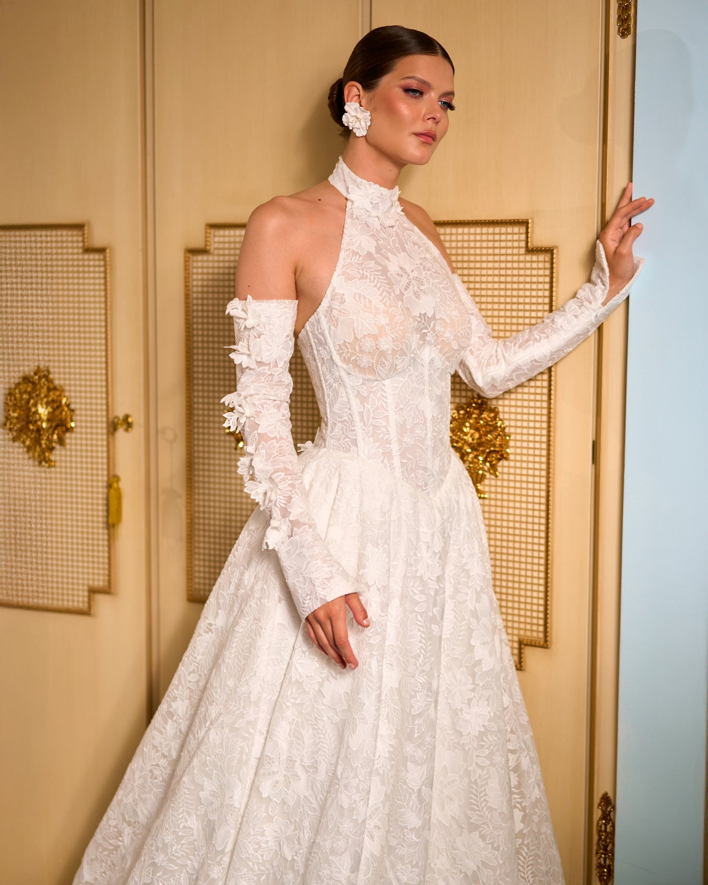 Lace A-line halter wedding dress with long removable sleeves adorned with 3D flowers, drop-down waist waspie corset, open lace-up back, and flowing chapel train for romantic bridal look