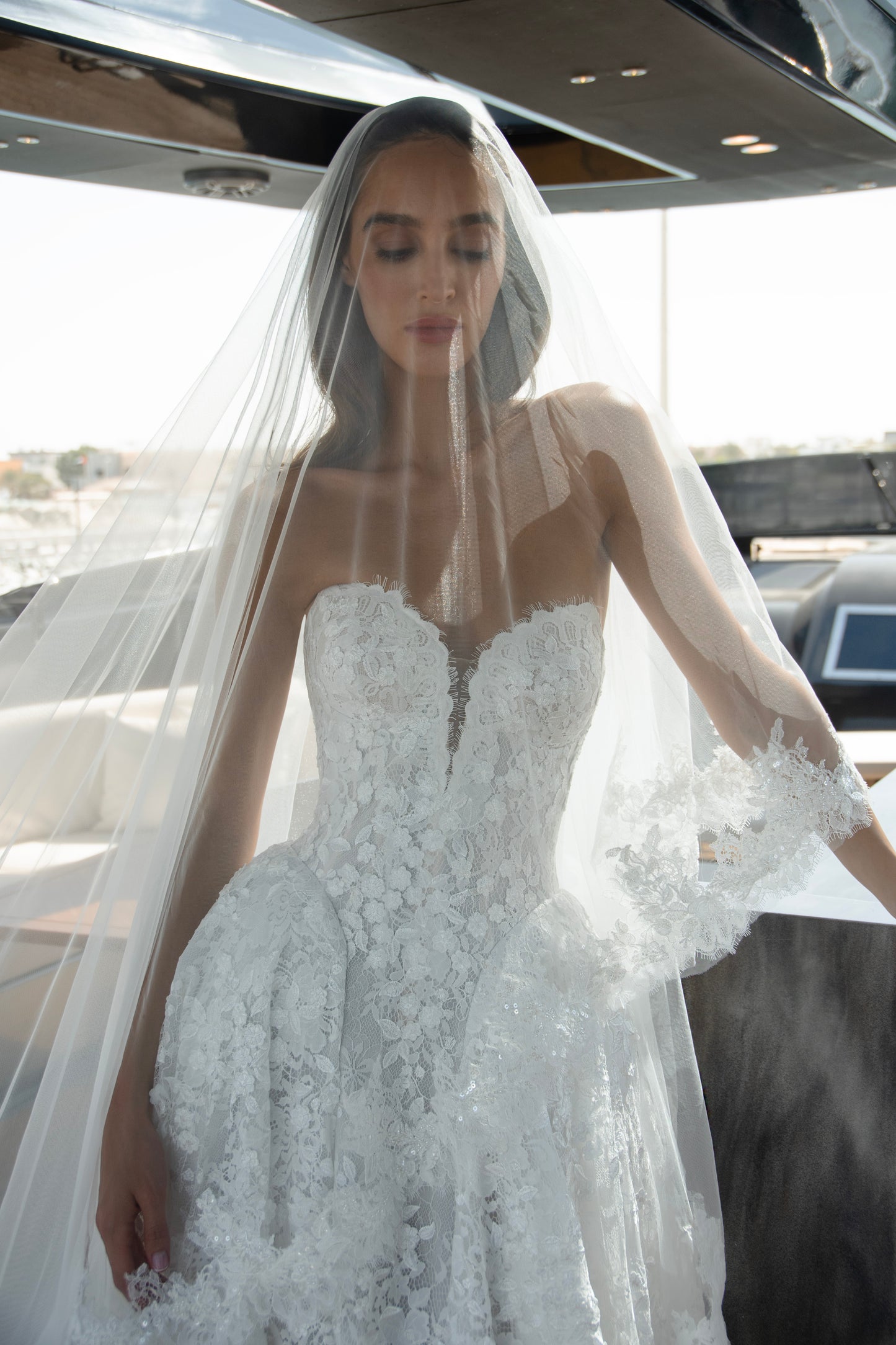 Bride wearing a high-neck lace wedding gown with long bell sleeves and chapel train from the Celeste Collection, photographed on a yacht.