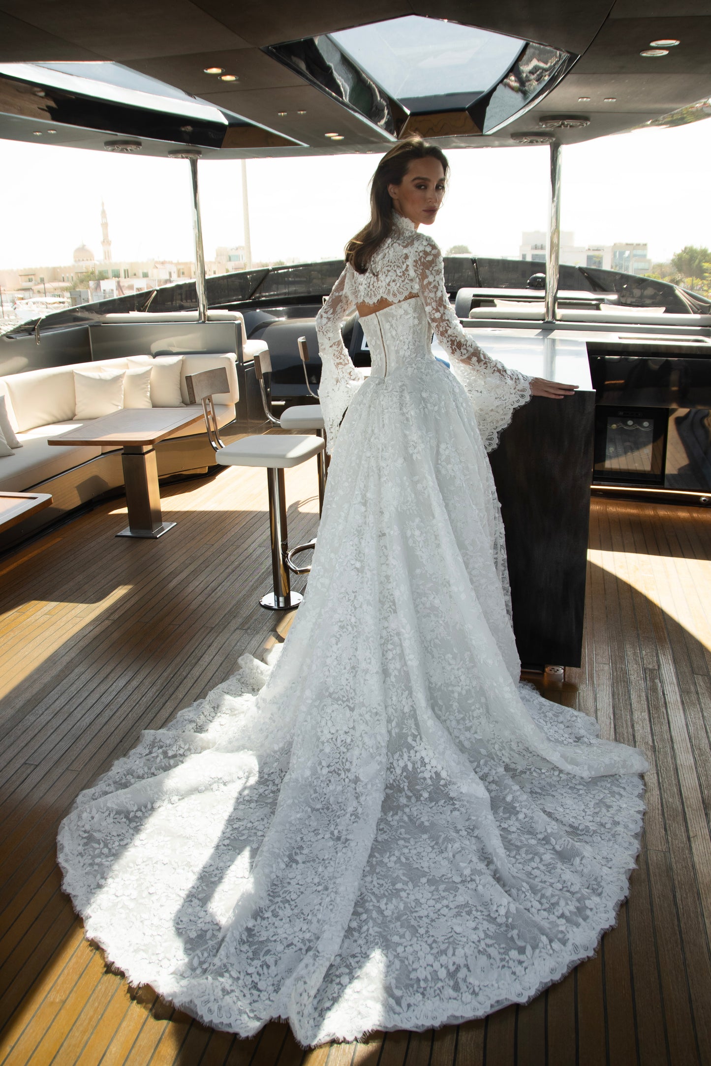 Bride wearing a high-neck lace wedding gown with long bell sleeves and chapel train from the Celeste Collection, photographed on a yacht.