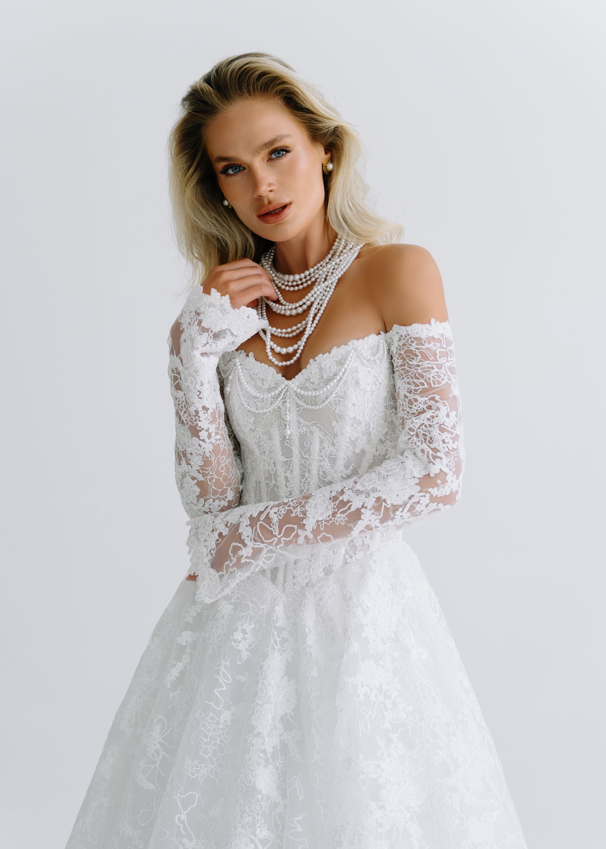 Close-up of an off-shoulder lace corset with long sleeves, styled with a pearl necklace