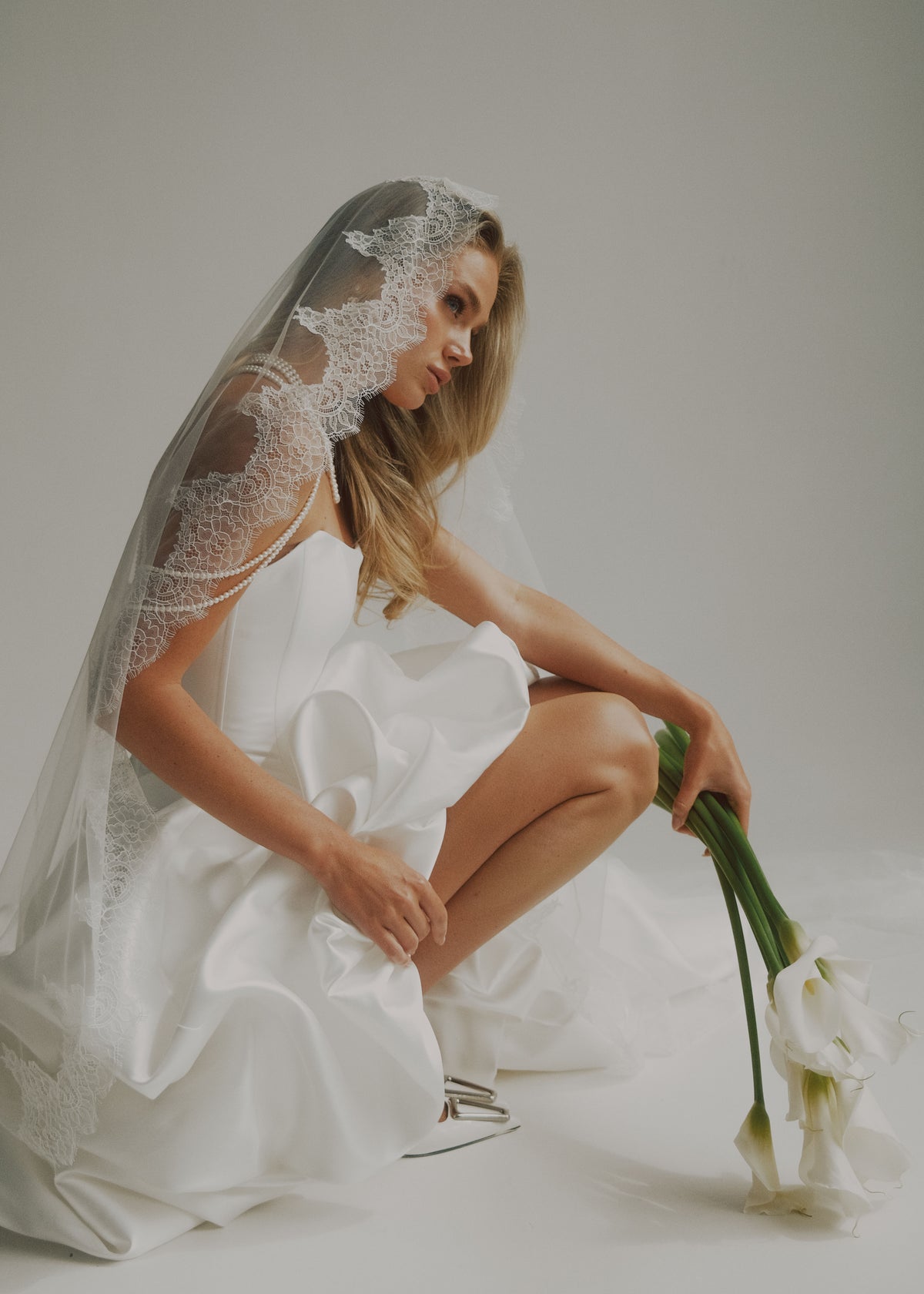 Bride in a short satin corset dress with a lace-trimmed veil, holding calla lilies