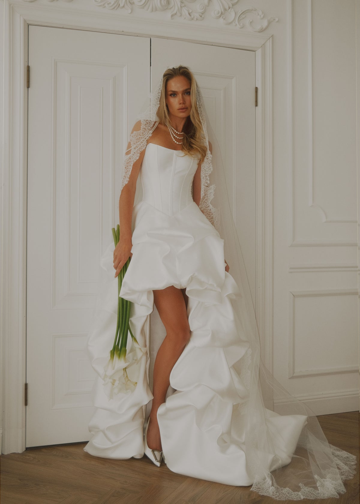 Full-length view of a satin high-low dress with a long ruffled train, in a bright interior