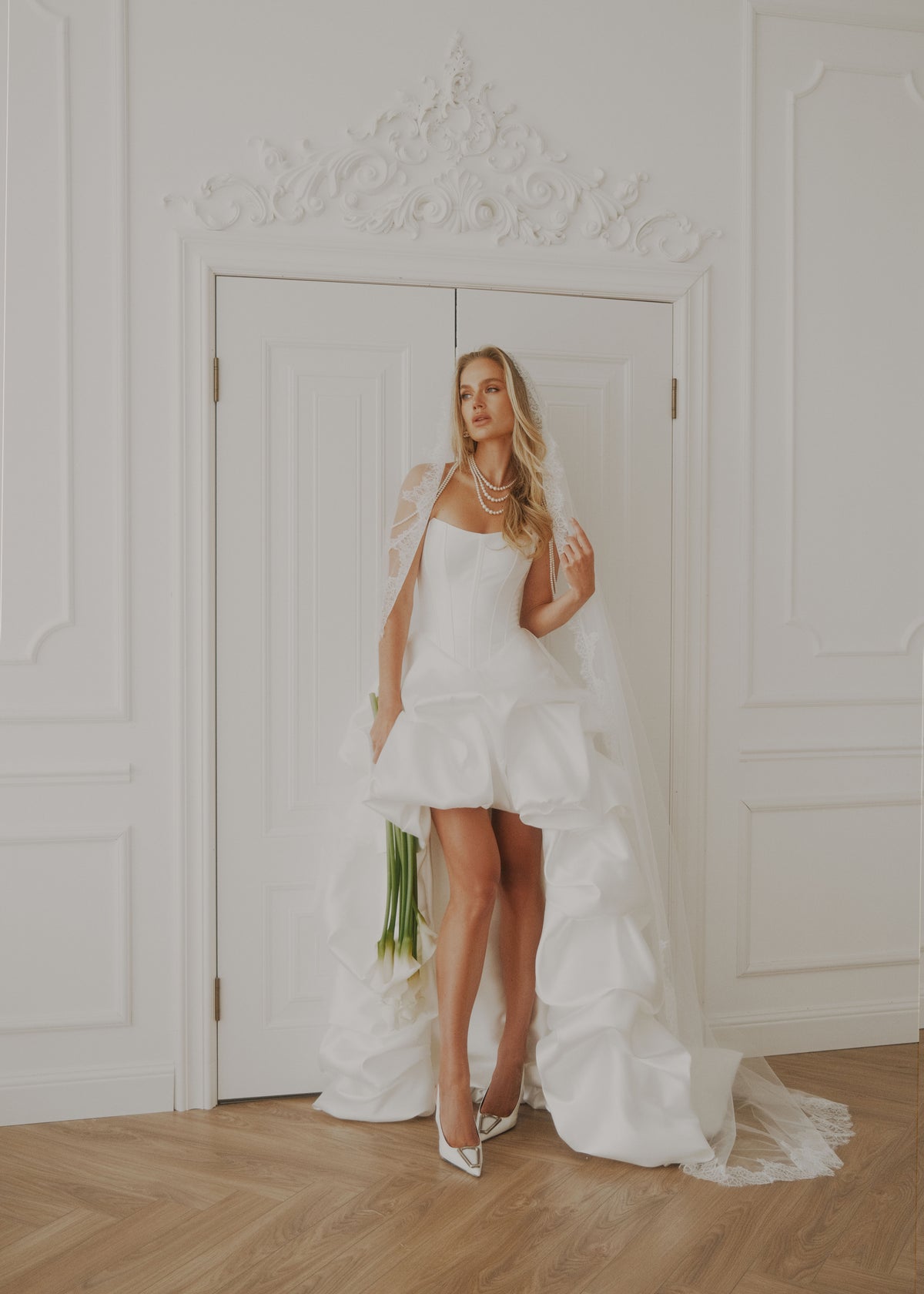Same short ruffled satin dress with a lace-trimmed veil, standing in a doorway