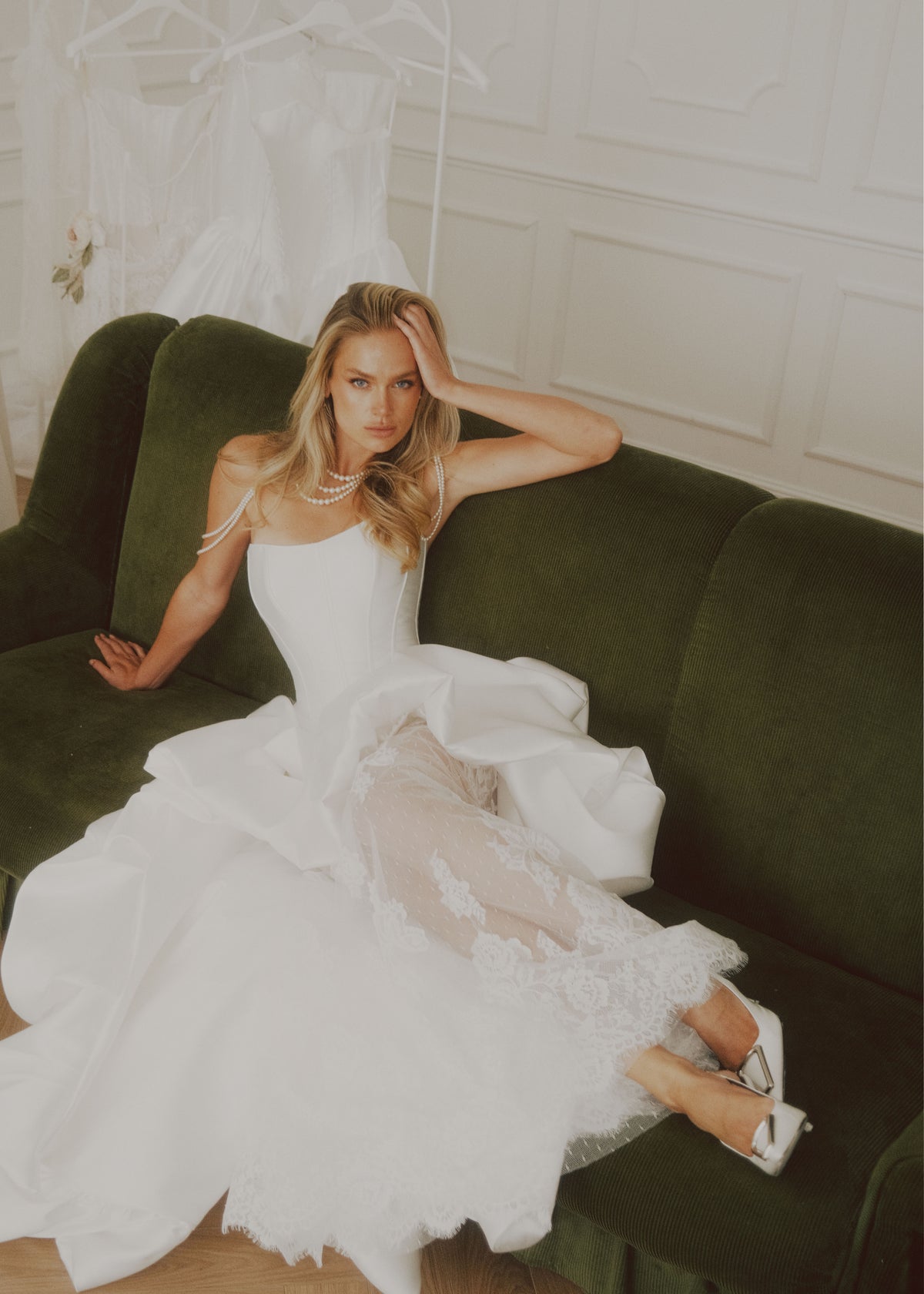 Bride on a green velvet sofa in a satin dress with a ruffled skirt over sheer lace