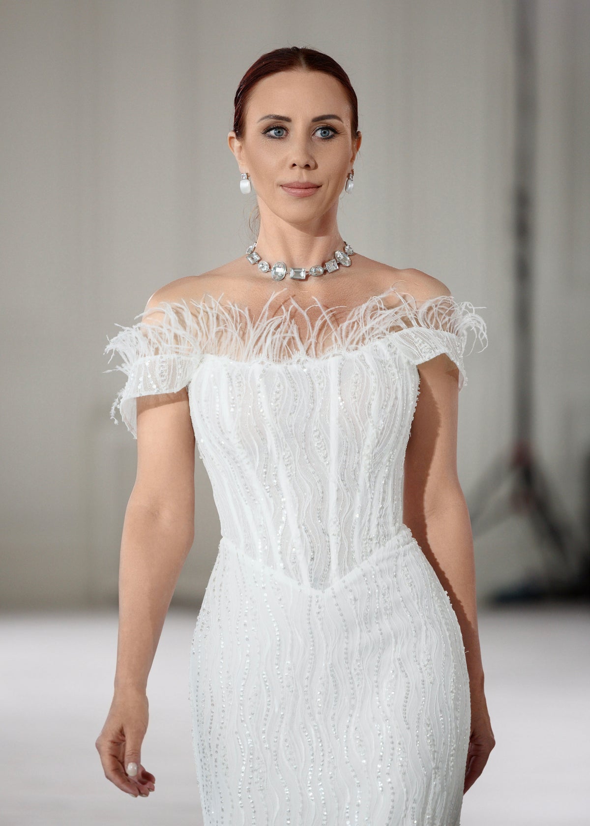 Model walking in a sequin lace wedding dress with an off-shoulder feather-trimmed neckline