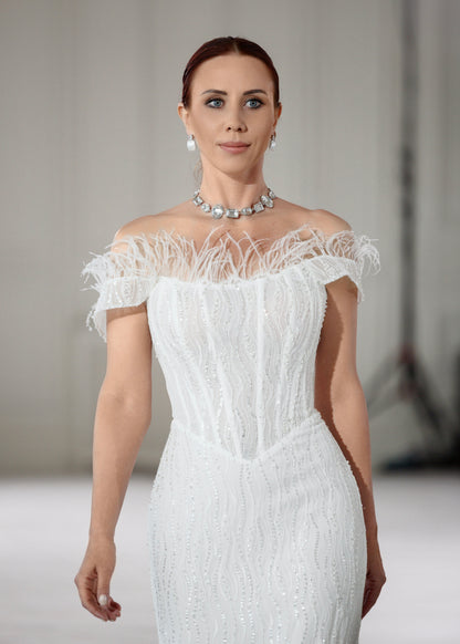 Model walking in a sequin lace wedding dress with an off-shoulder feather-trimmed neckline