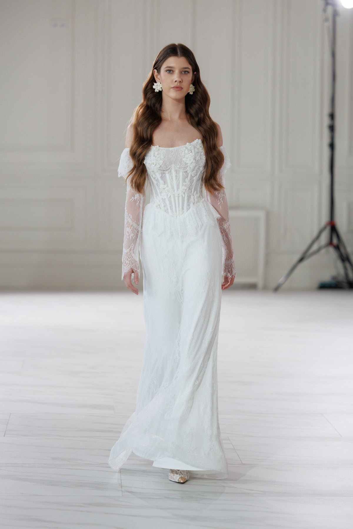 Model walking in a lace fit-and-flare wedding dress in a bright studio