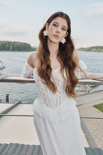 Portrait by the water of a lace corset bodice with sheer sleeves