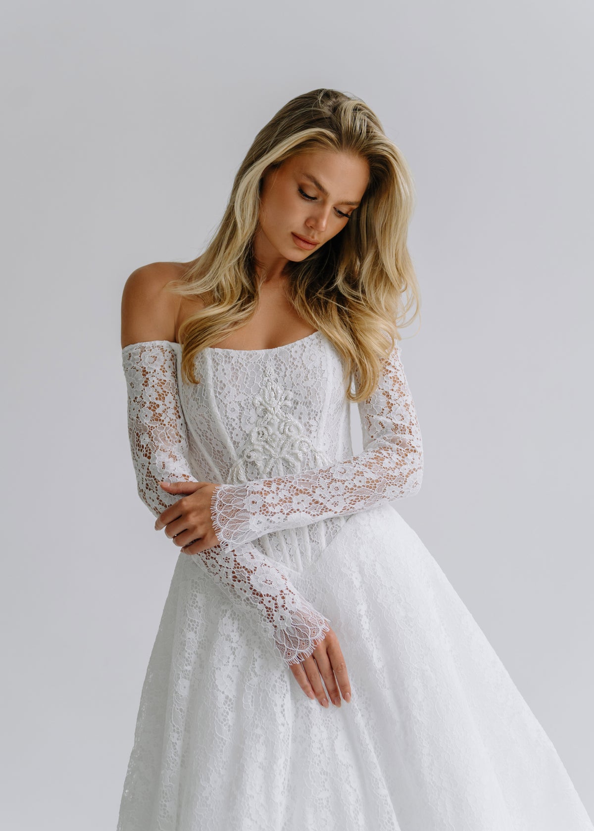 Bride looking down in a lace off-shoulder wedding dress with long sleeves