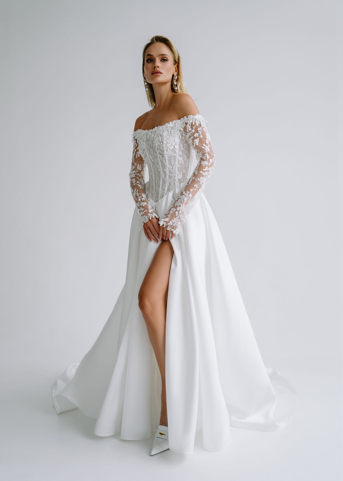 Satin A-line wedding dress with an off-shoulder lace corset, long lace sleeves and a high slit, front view
