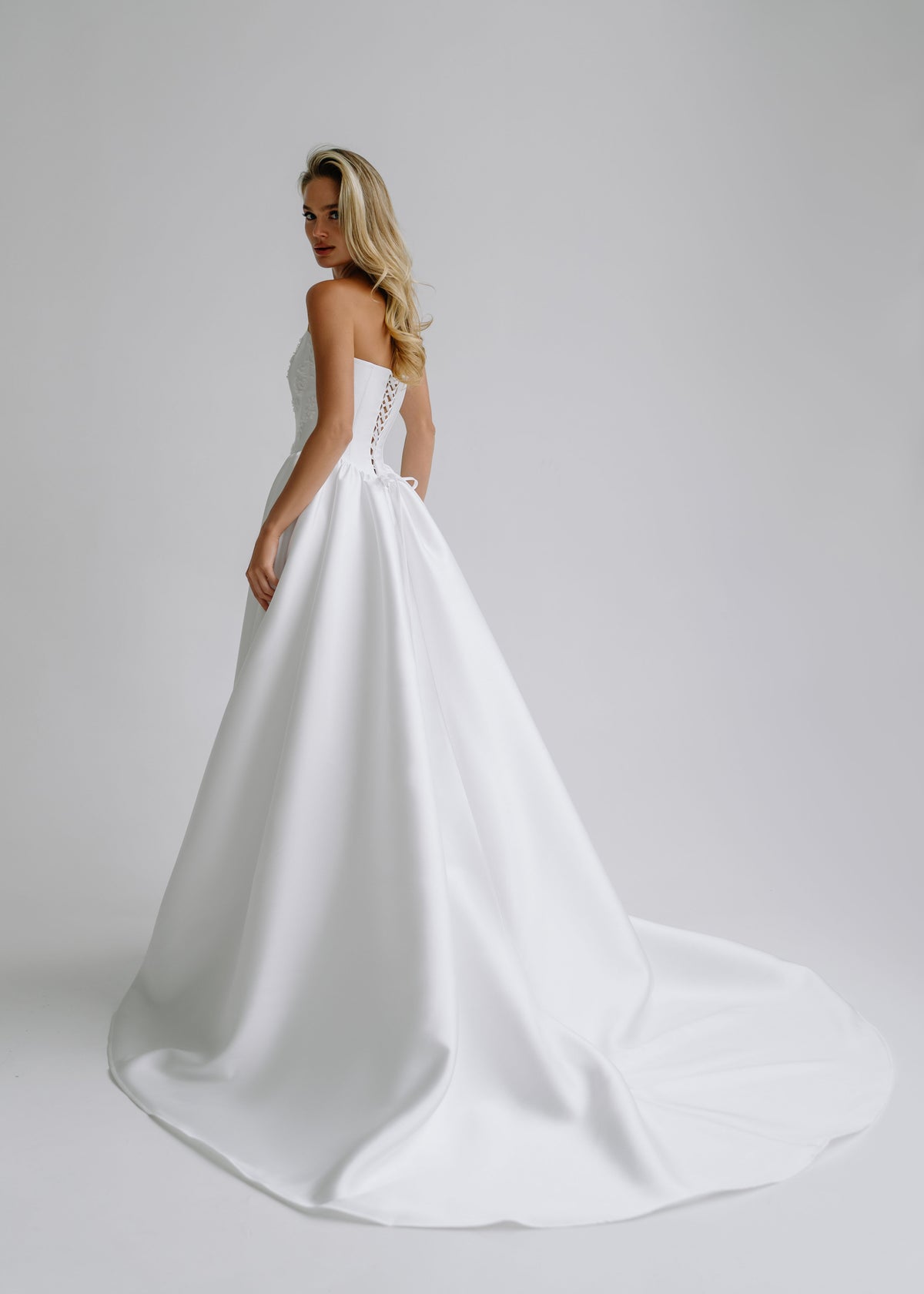 Back view of a satin wedding dress with a lace-up back and a train