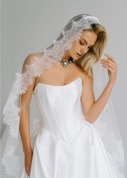 Close-up of a strapless satin corset bodice with a scalloped lace-trimmed veil