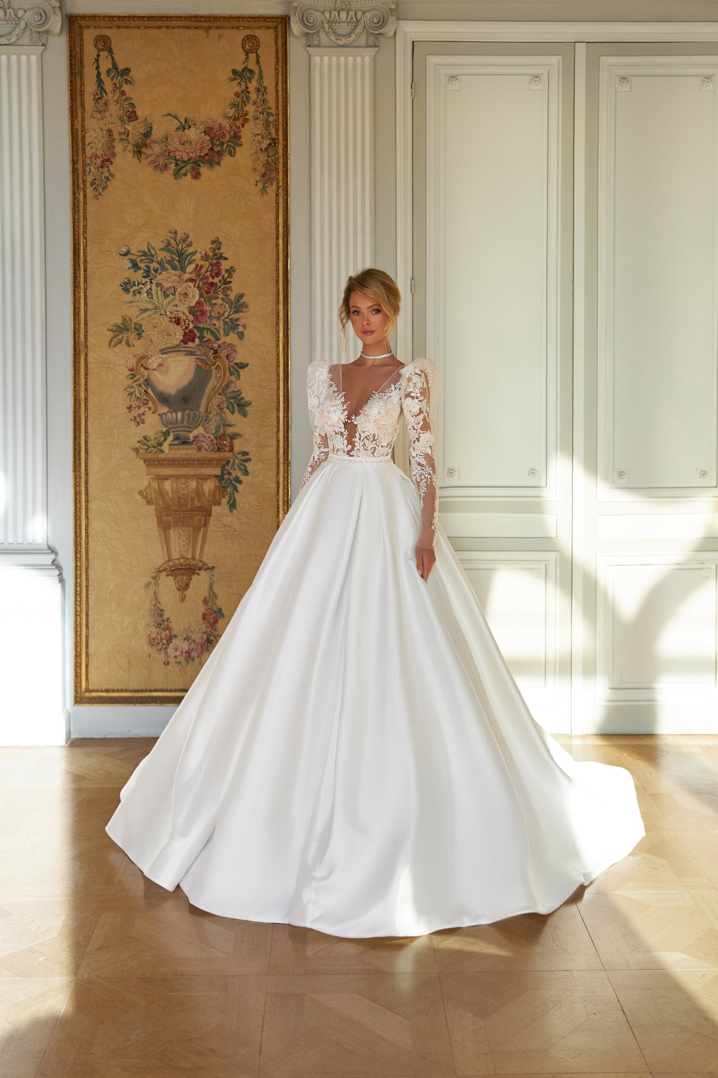  A-line wedding dress with puffy shoulder sleeves, V-shaped bodice, pleated skirt with pockets, embroidered belt, lace appliques, sequin details, and chapel train. Made of lace and taffeta mikado.