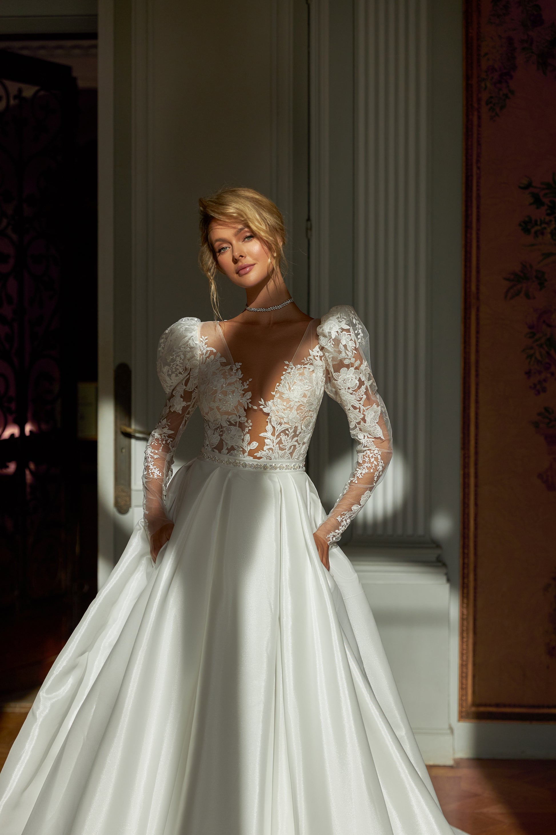  A-line wedding dress with puffy shoulder sleeves, V-shaped bodice, pleated skirt with pockets, embroidered belt, lace appliques, sequin details, and chapel train. Made of lace and taffeta mikado.