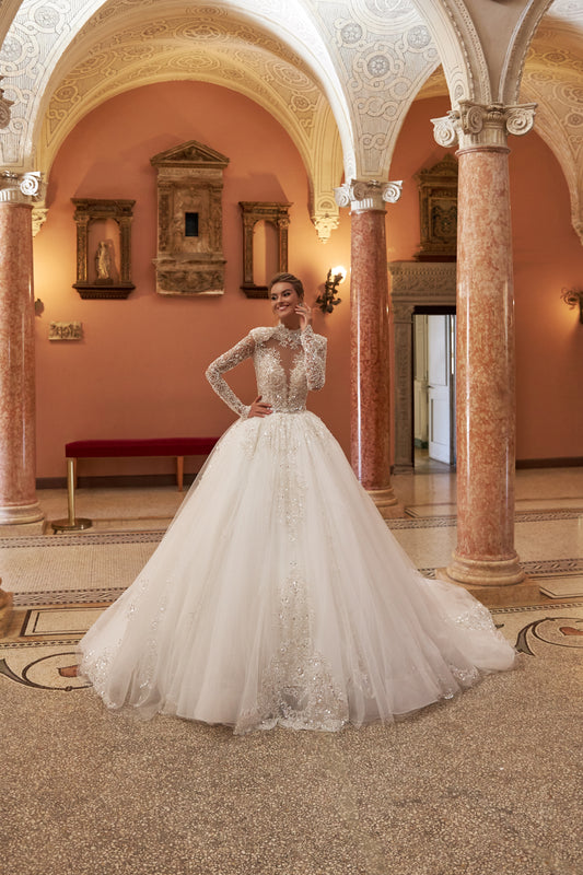 Princess Ball Gown wedding dress with halter neckline, sleeveless bodice, open back, long-sleeve mockneck cape, lace appliques, and cathedral train. Embellished with silver and transparent beads and sequins.