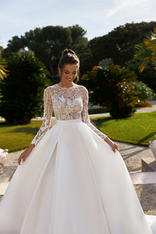 A-line bridal gown with long sleeves, pleated skirt, detachable belt, Chantilly lace, bead and sequin embroidery, and chapel train.