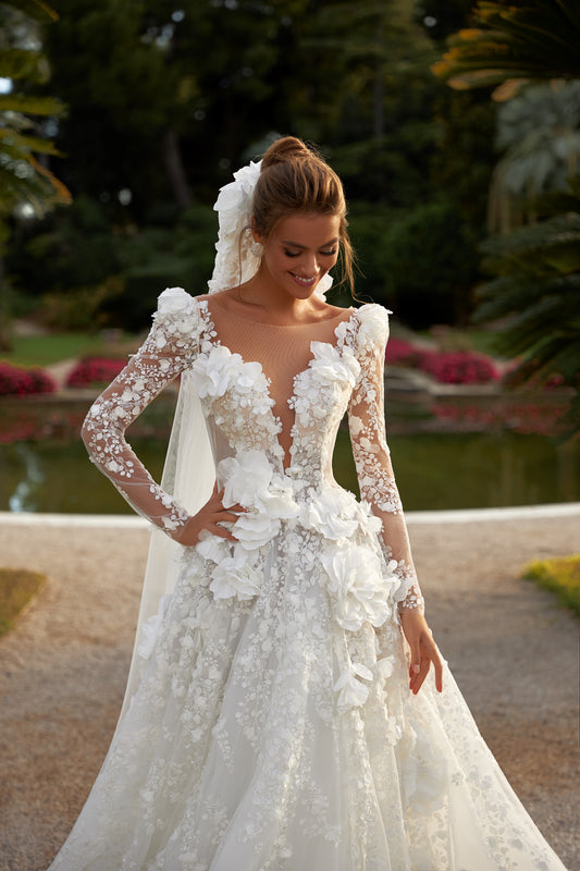 A-line wedding dress with long illusion sleeves, deep halter V-neckline, open back, lace appliques, handmade flowers, pearl and sequin embroidery, and a glittering tulle chapel train.