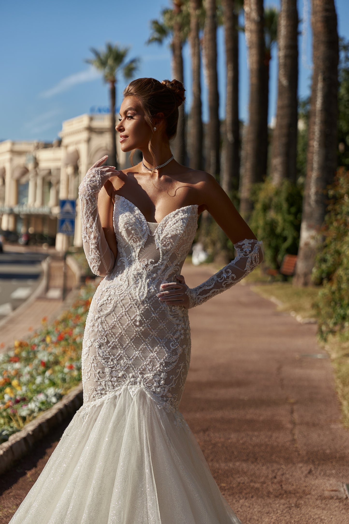 Mermaid silhouette wedding dress with V-neckline, open back, removable gloves, lace appliques, bead and sequin embroidery, and a fishtail train. Made from lace and tulle.