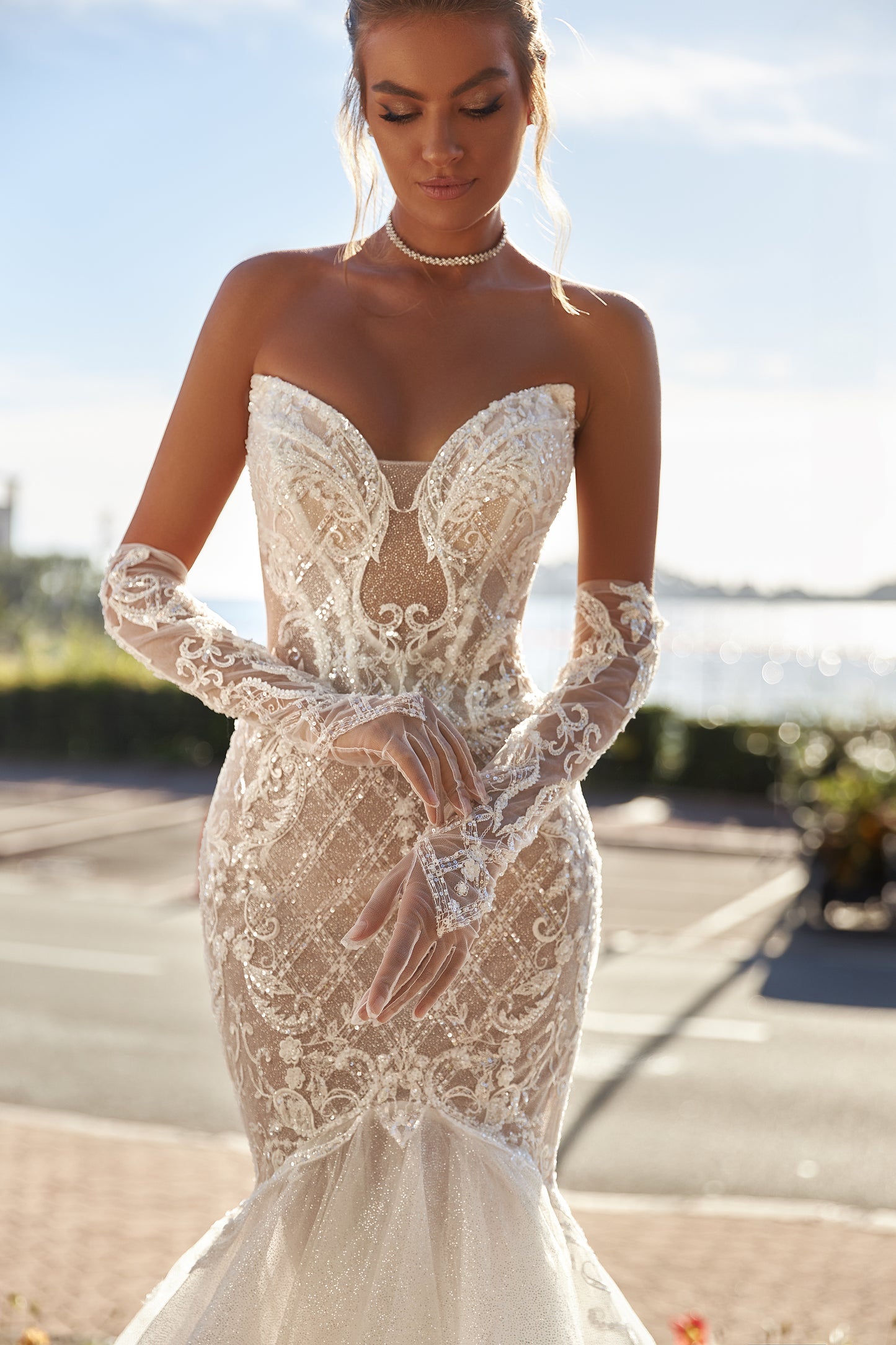 Mermaid silhouette wedding dress with V-neckline, open back, removable gloves, lace appliques, bead and sequin embroidery, and a fishtail train. Made from lace and tulle.