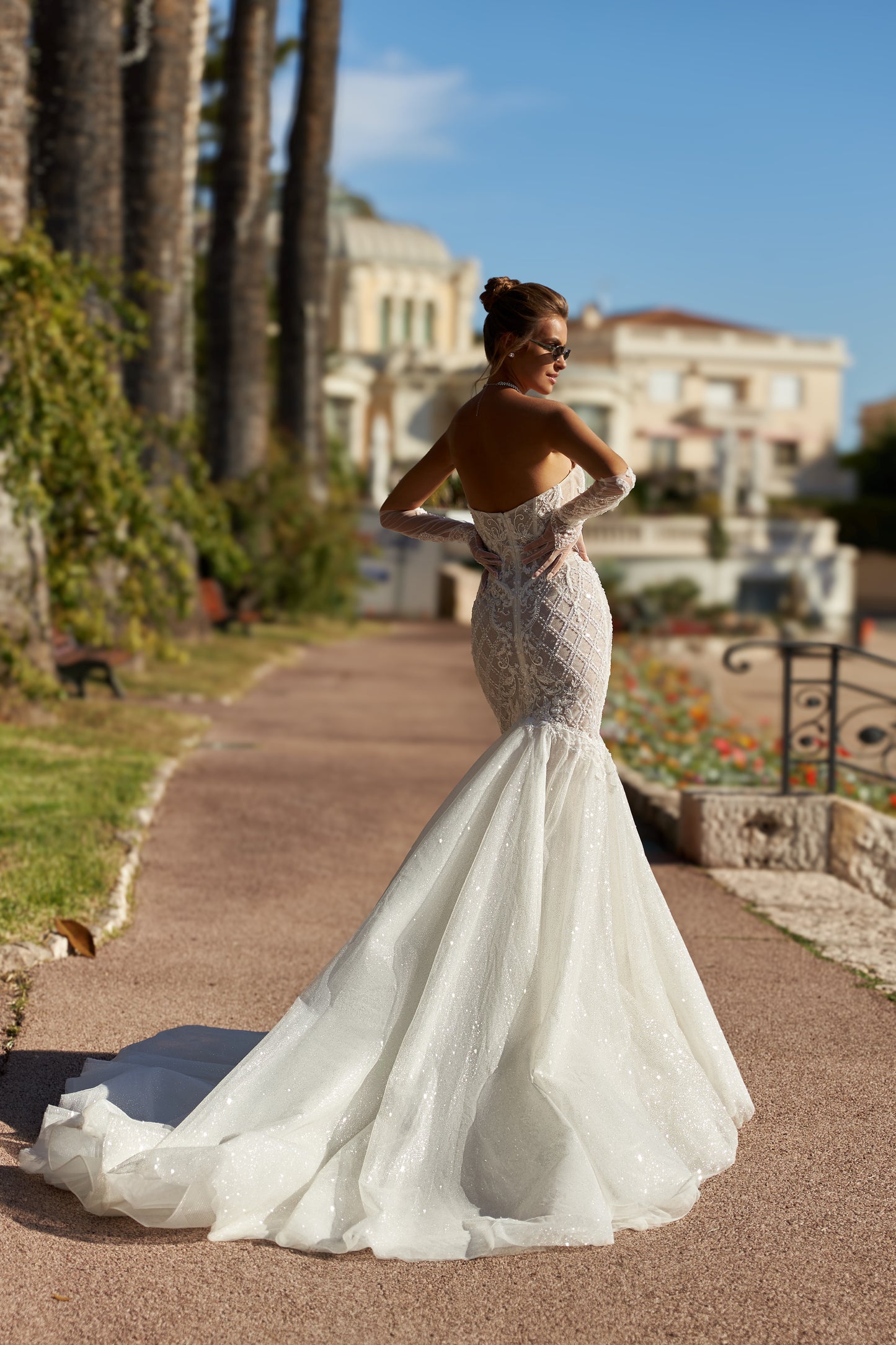 Mermaid silhouette wedding dress with V-neckline, open back, removable gloves, lace appliques, bead and sequin embroidery, and a fishtail train. Made from lace and tulle.