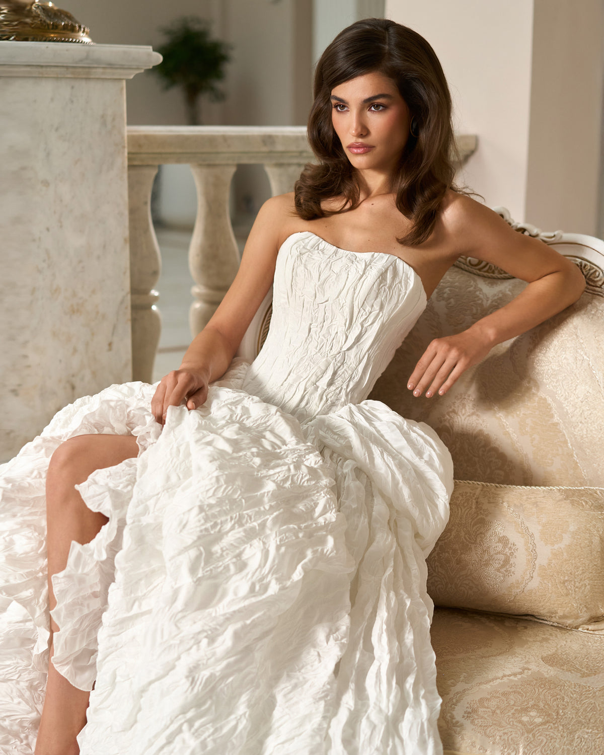 Seated close-up of the strapless sweetheart bodice and sculpted waist of a white textured taffeta wedding dress.