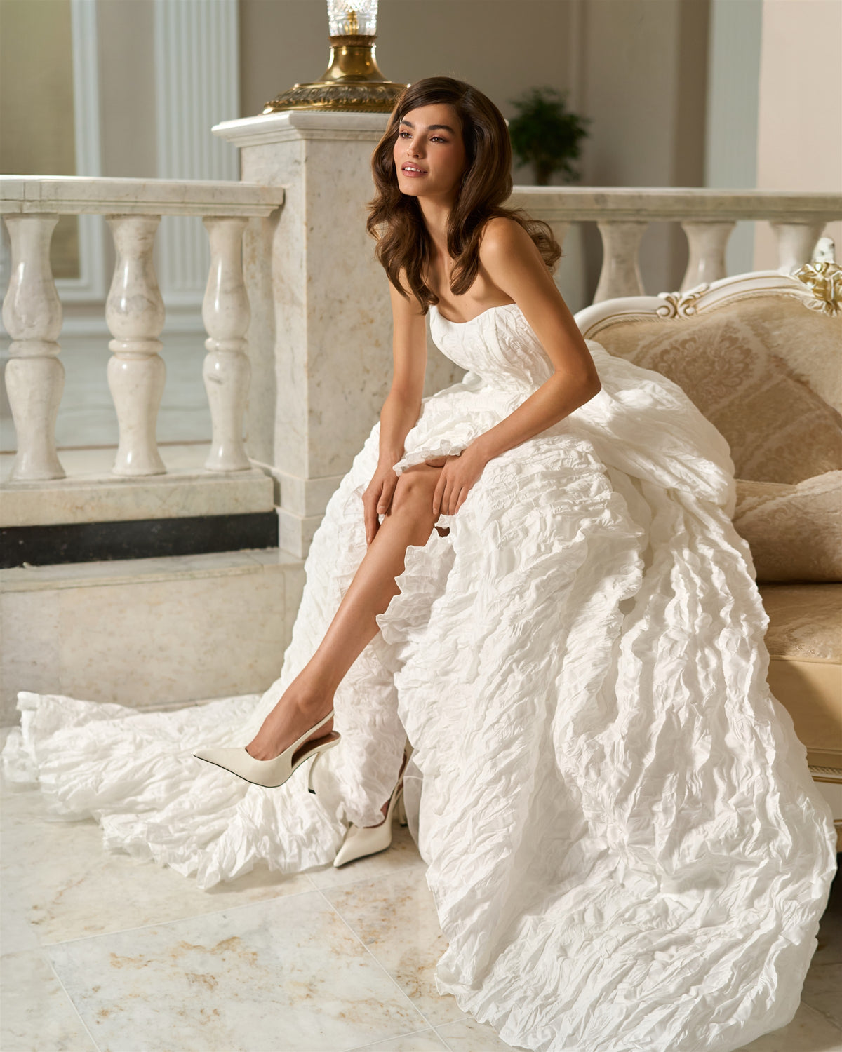 Side view of a seated bride wearing a white textured taffeta wedding dress with an open front skirt and flowing train.