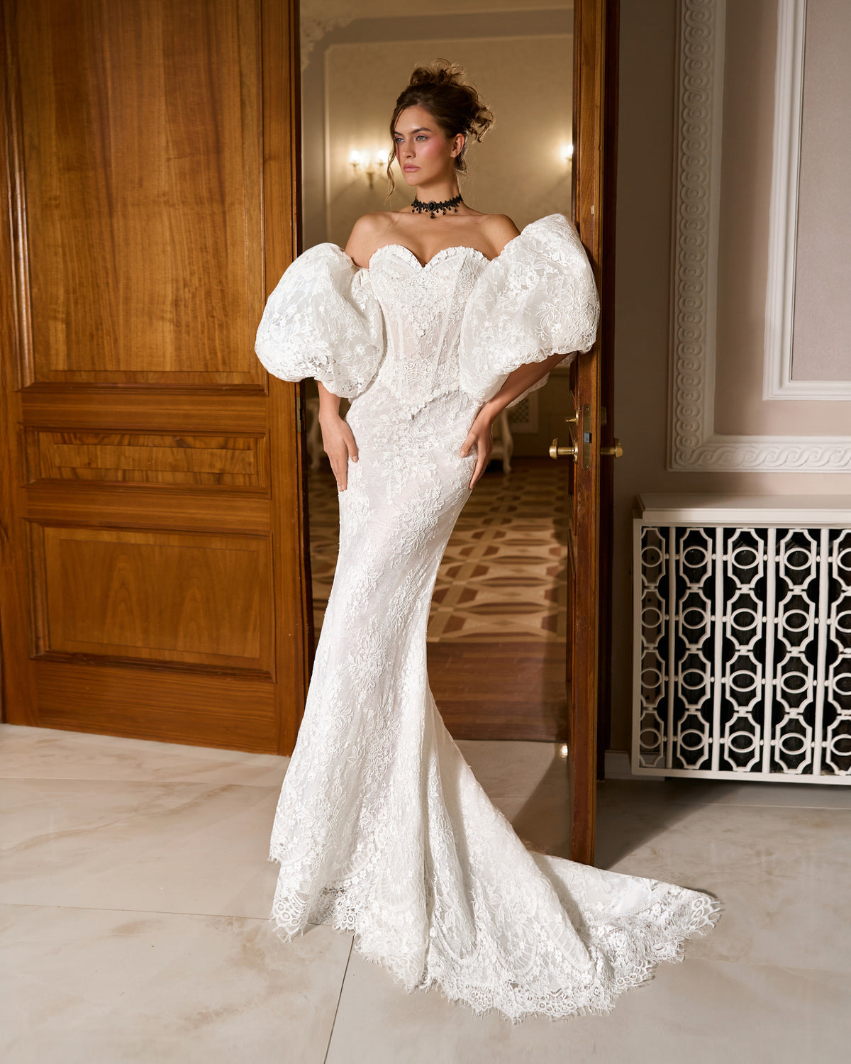 Mermaid lace wedding dress with sweetheart corset bodice and large puffy sleeves, standing in a doorway