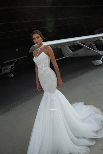 Strapless mermaid wedding dress with corrugated tulle, pearl detailing, fit and flare silhouette, and sweeping fishtail train for striking modern bridal look