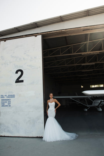 Strapless mermaid wedding dress with corrugated tulle, pearl detailing, fit and flare silhouette, and sweeping fishtail train for striking modern bridal look