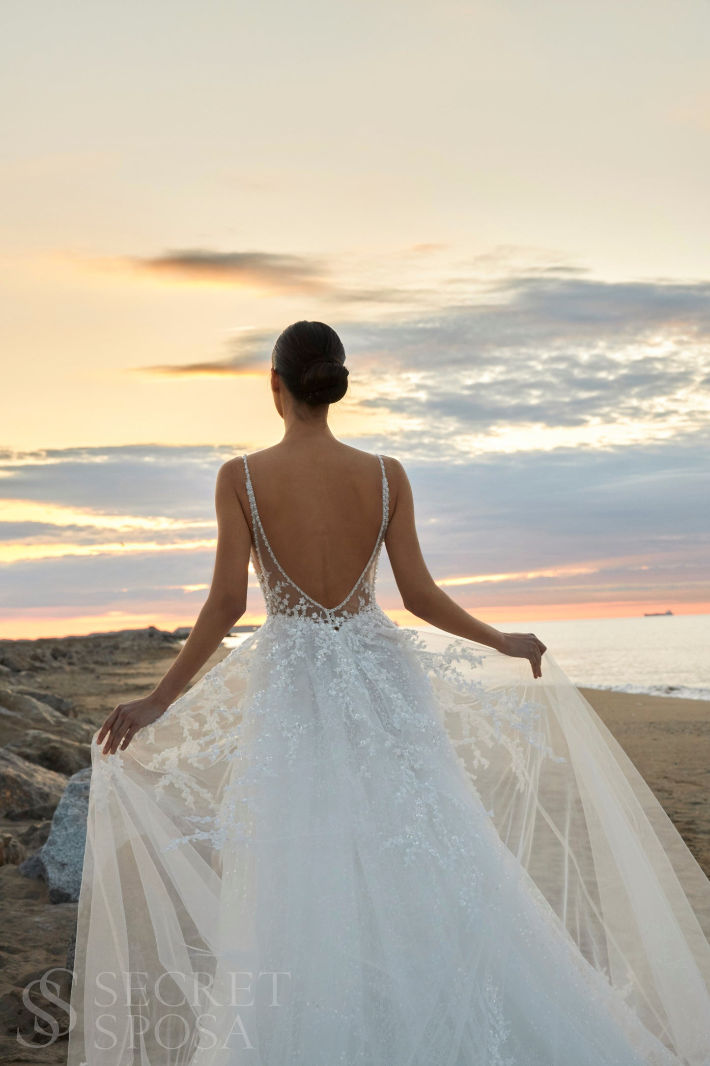 Bride in A-line halter wedding dress with spaghetti straps, sequin embroidered lace tulle skirt, high slit, and open back.