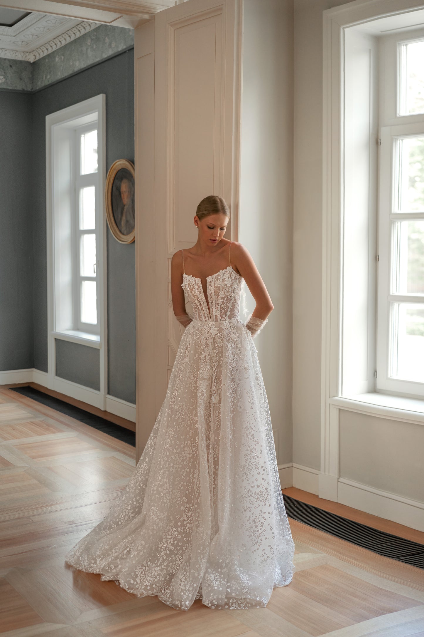 Romantic sleeveless wedding dress with thin spaghetti straps, deep V-neckline, and glitter lace detailing.