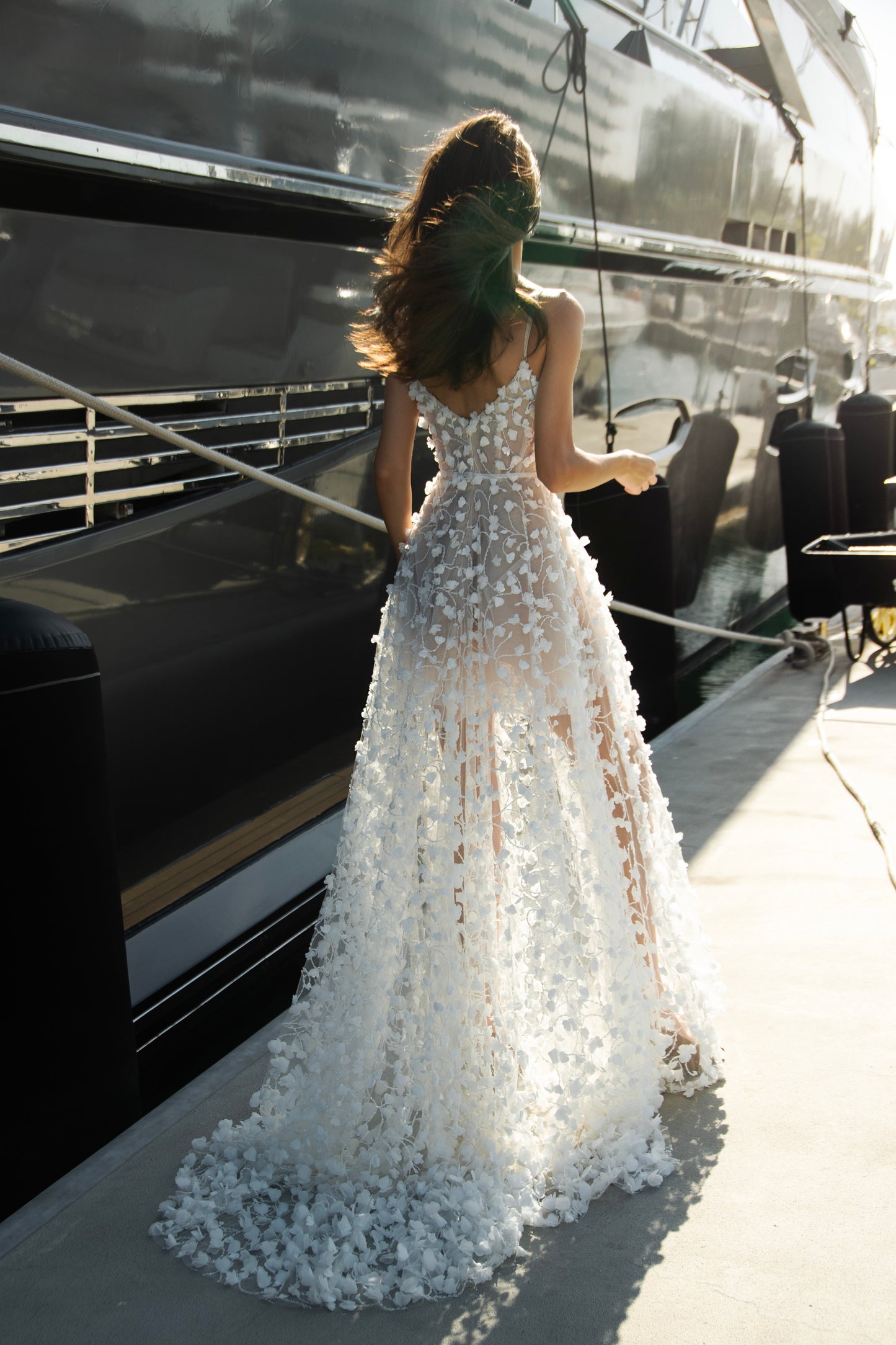 Bride wearing a sheer tulle A-line wedding gown with 3D floral appliqués from the Celeste Collection, photographed by a yacht.