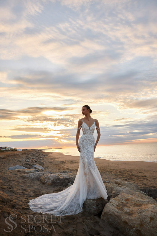 Bride in mermaid fit-and-flare lace wedding dress with pearl spaghetti straps, off-the-shoulder pearl strands, V-neckline, and sweep train.