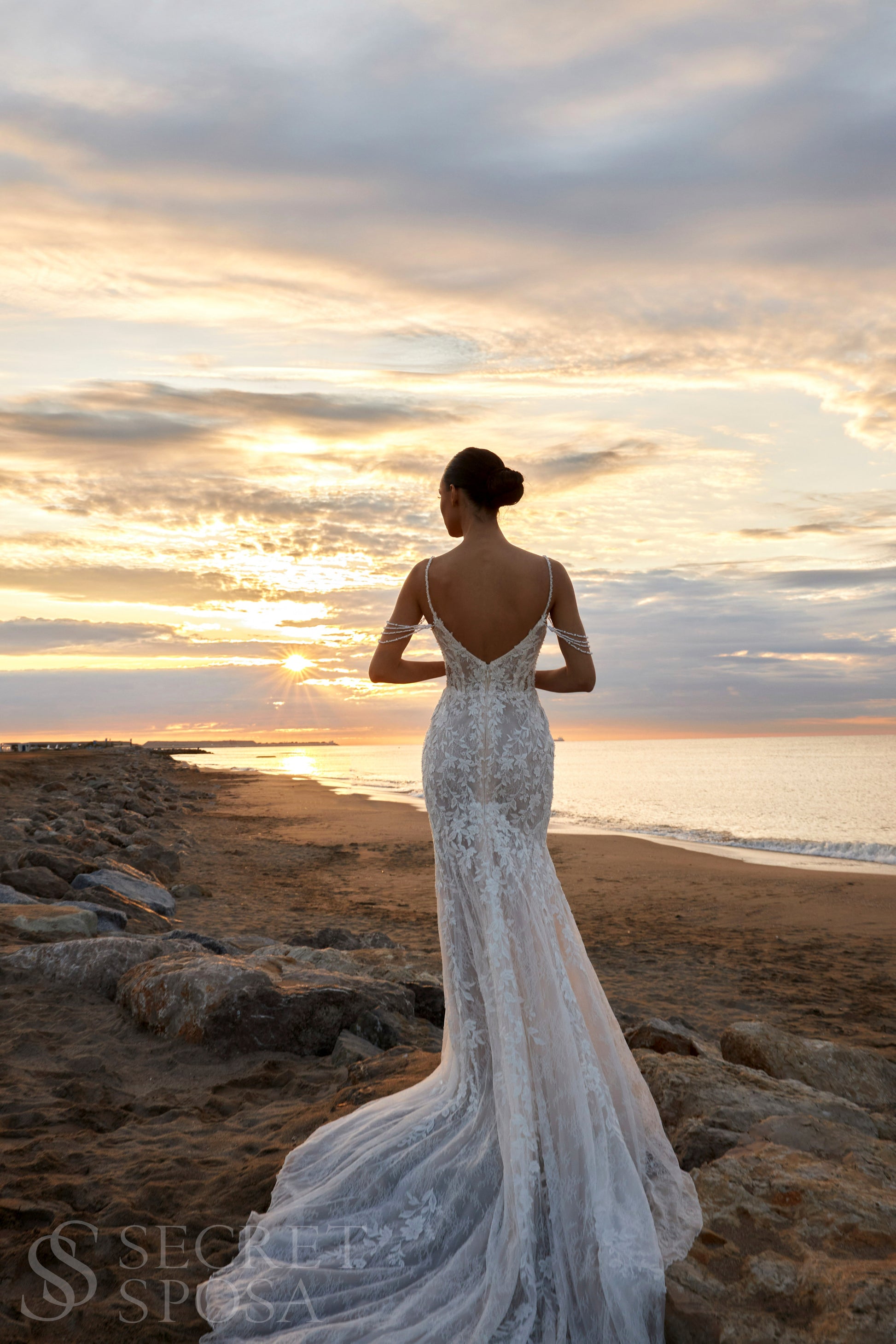 Bride in mermaid fit-and-flare lace wedding dress with pearl spaghetti straps, off-the-shoulder pearl strands, V-neckline, and sweep train.