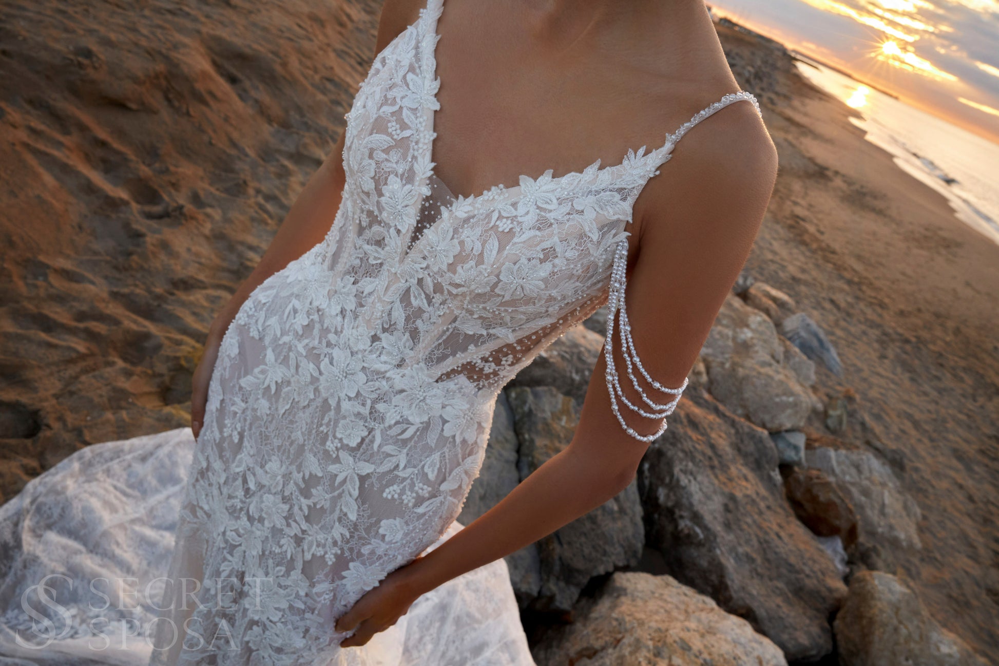 Bride in mermaid fit-and-flare lace wedding dress with pearl spaghetti straps, off-the-shoulder pearl strands, V-neckline, and sweep train.