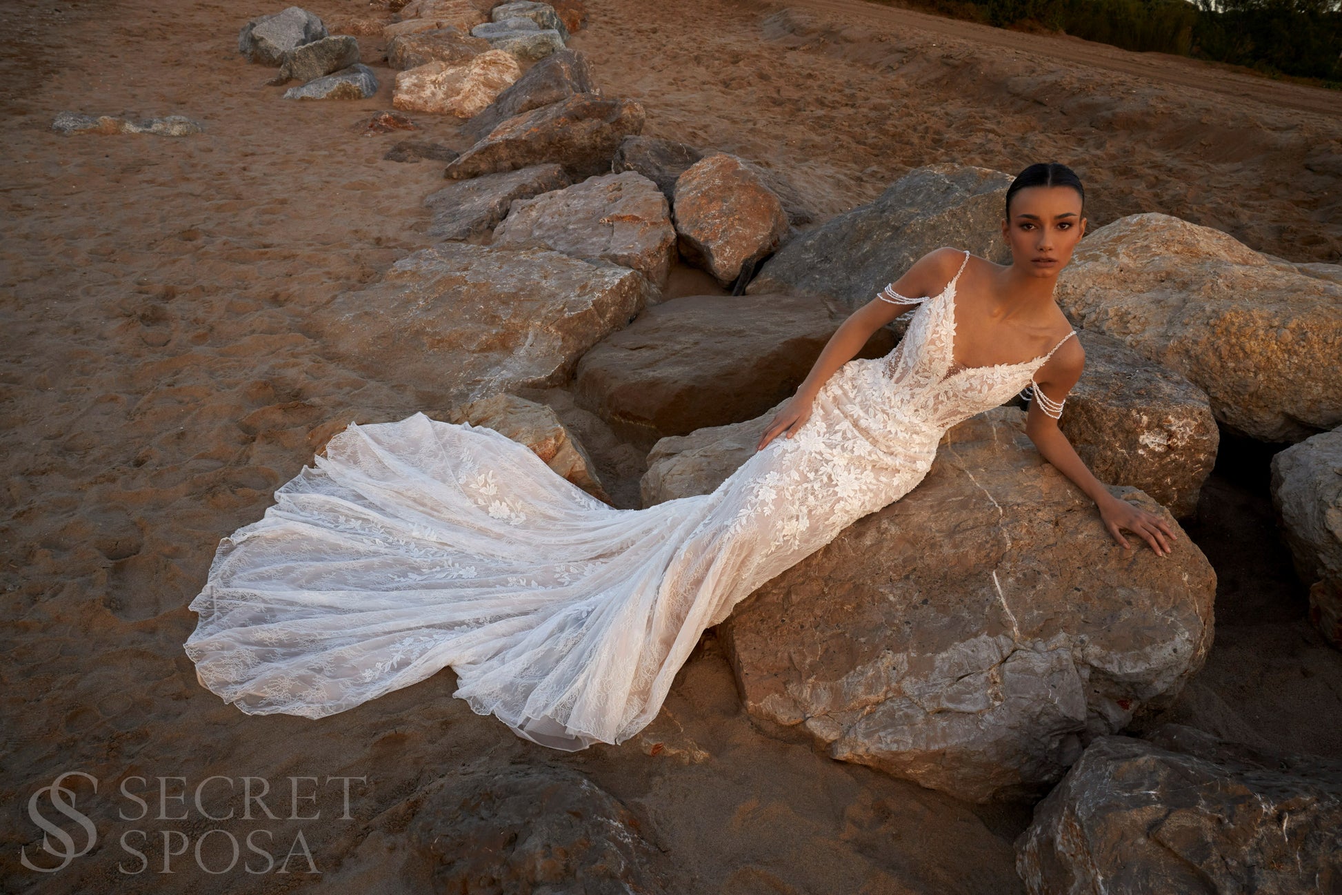 Bride in mermaid fit-and-flare lace wedding dress with pearl spaghetti straps, off-the-shoulder pearl strands, V-neckline, and sweep train.