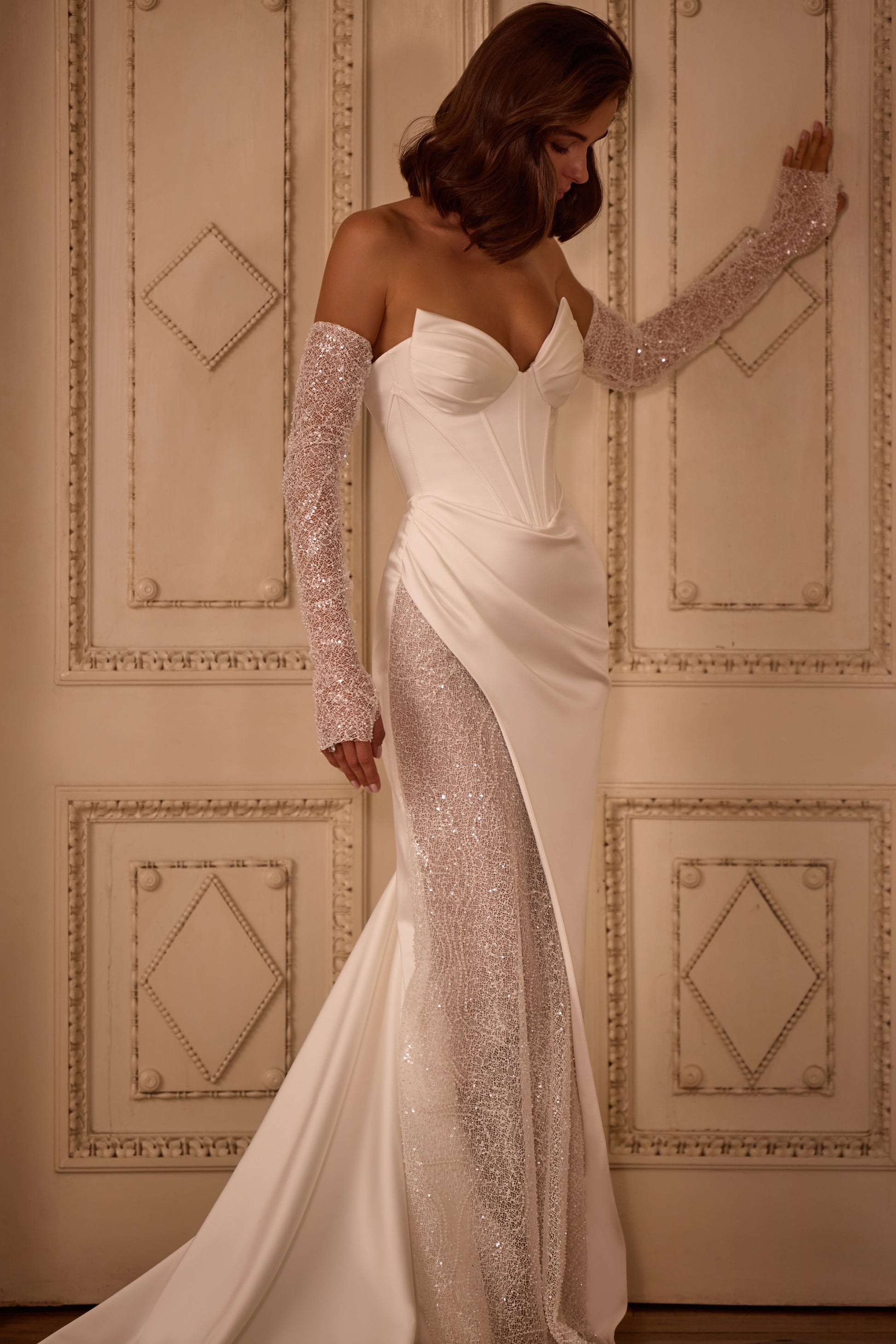 Bride wearing a modern wedding dress with lace-up corset, detachable sleeves, and a dramatic sweeping train, styled for ceremony and reception versatility.


