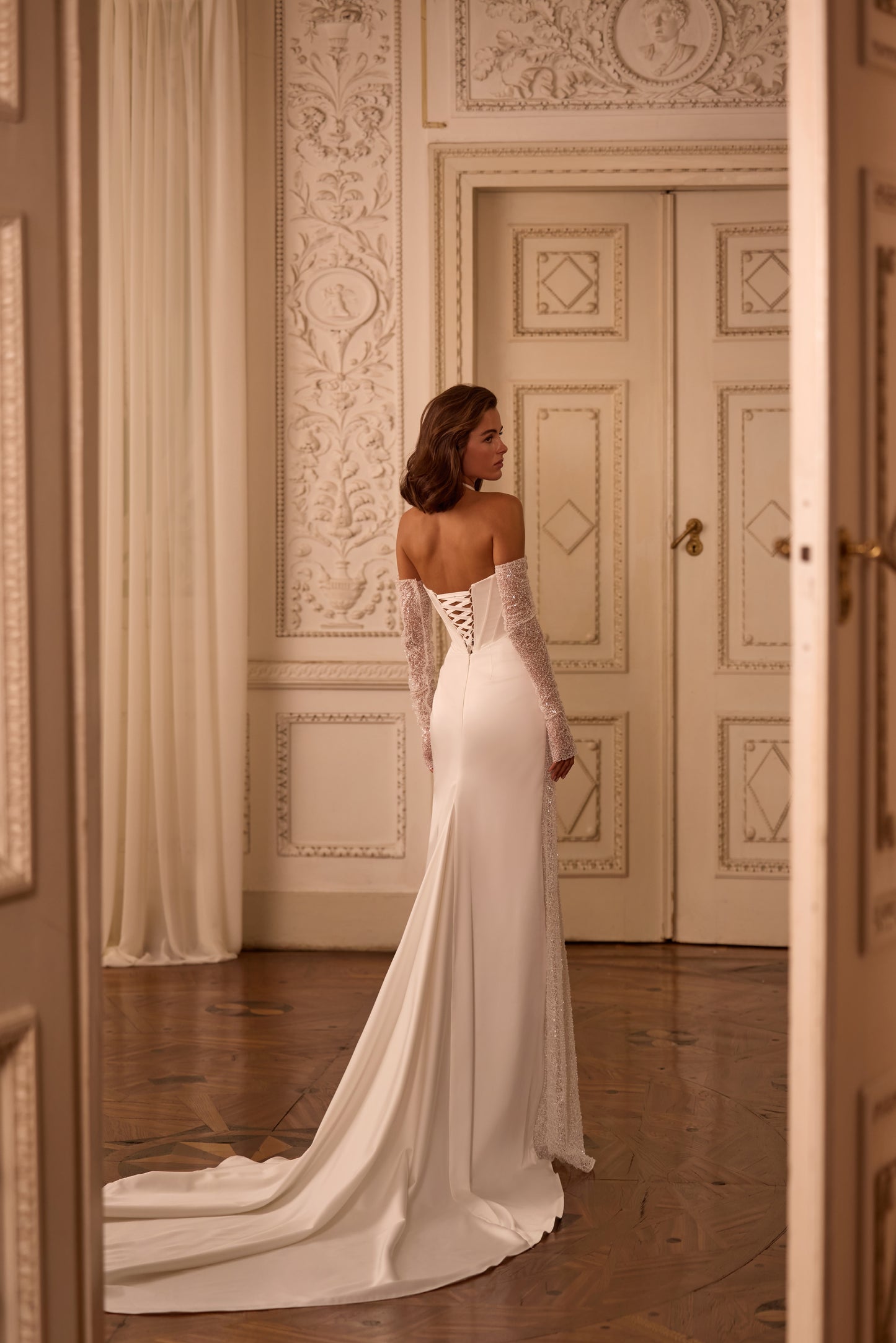 Bride wearing a modern wedding dress with lace-up corset, detachable sleeves, and a dramatic sweeping train, styled for ceremony and reception versatility.

