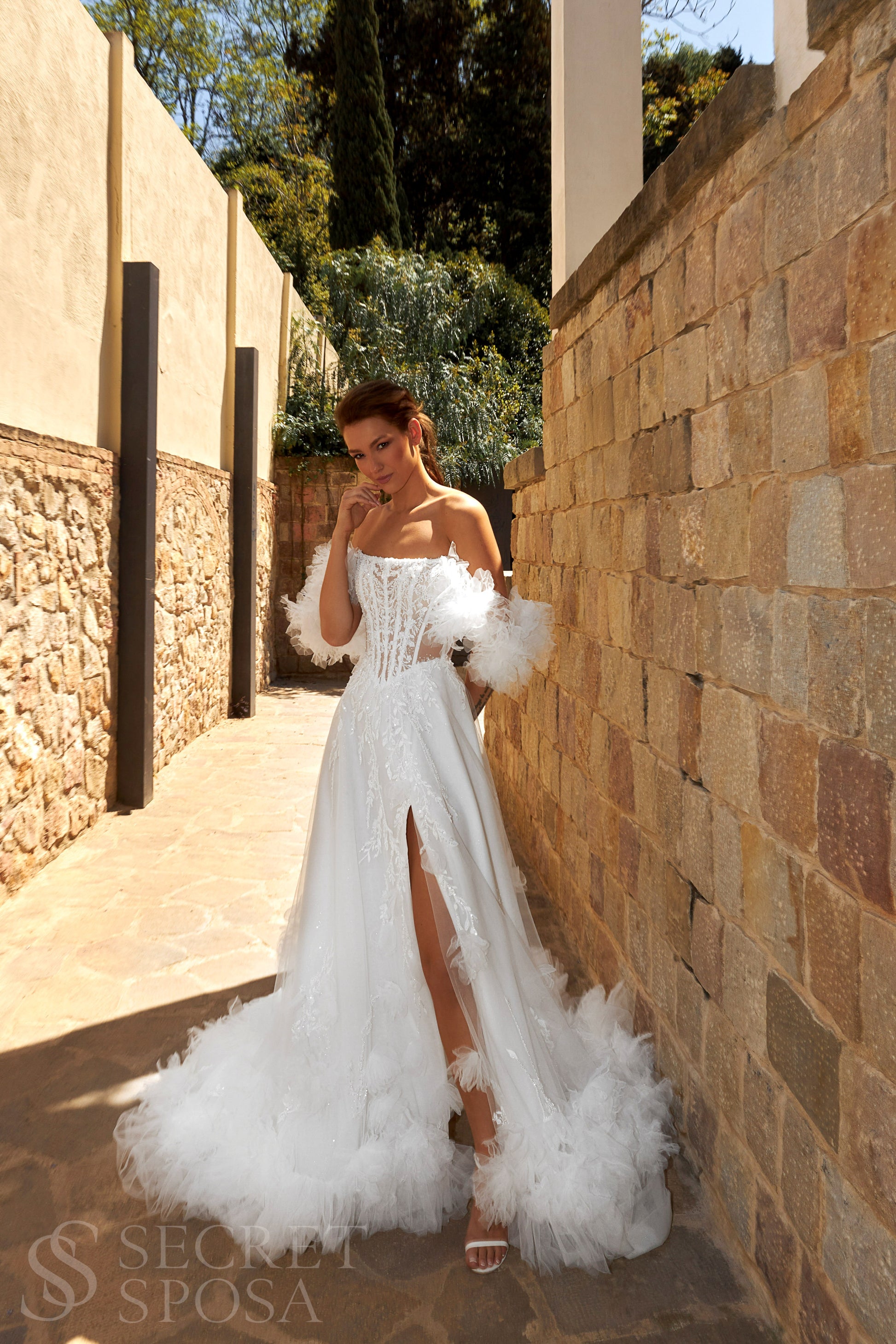 Bride in sleeveless tulle A-line wedding gown with pearl-adorned lace, 3D floral appliqués, boat neckline, slit skirt, drop waist, and straight open back.
