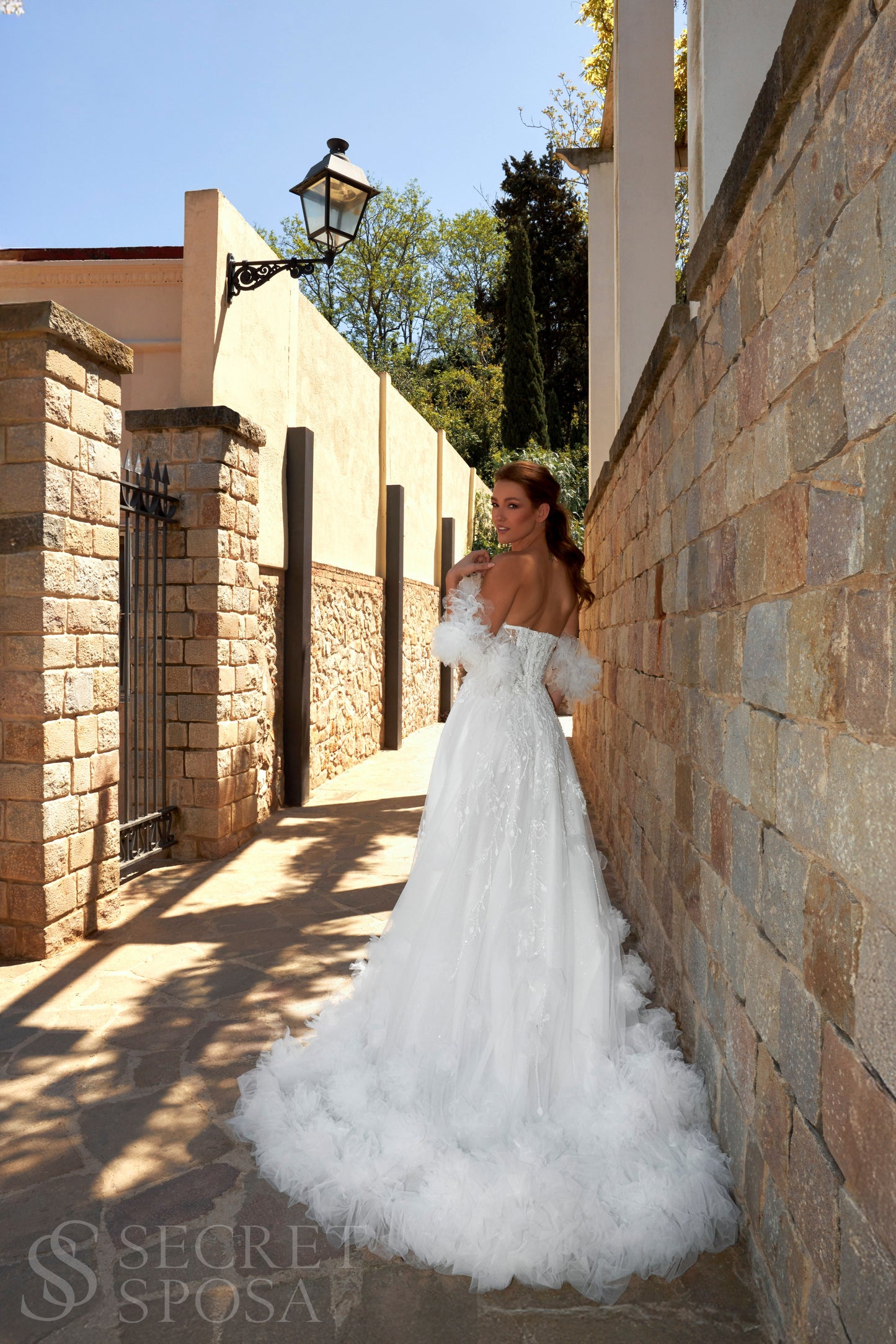 Bride in sleeveless tulle A-line wedding gown with pearl-adorned lace, 3D floral appliqués, boat neckline, slit skirt, drop waist, and straight open back.