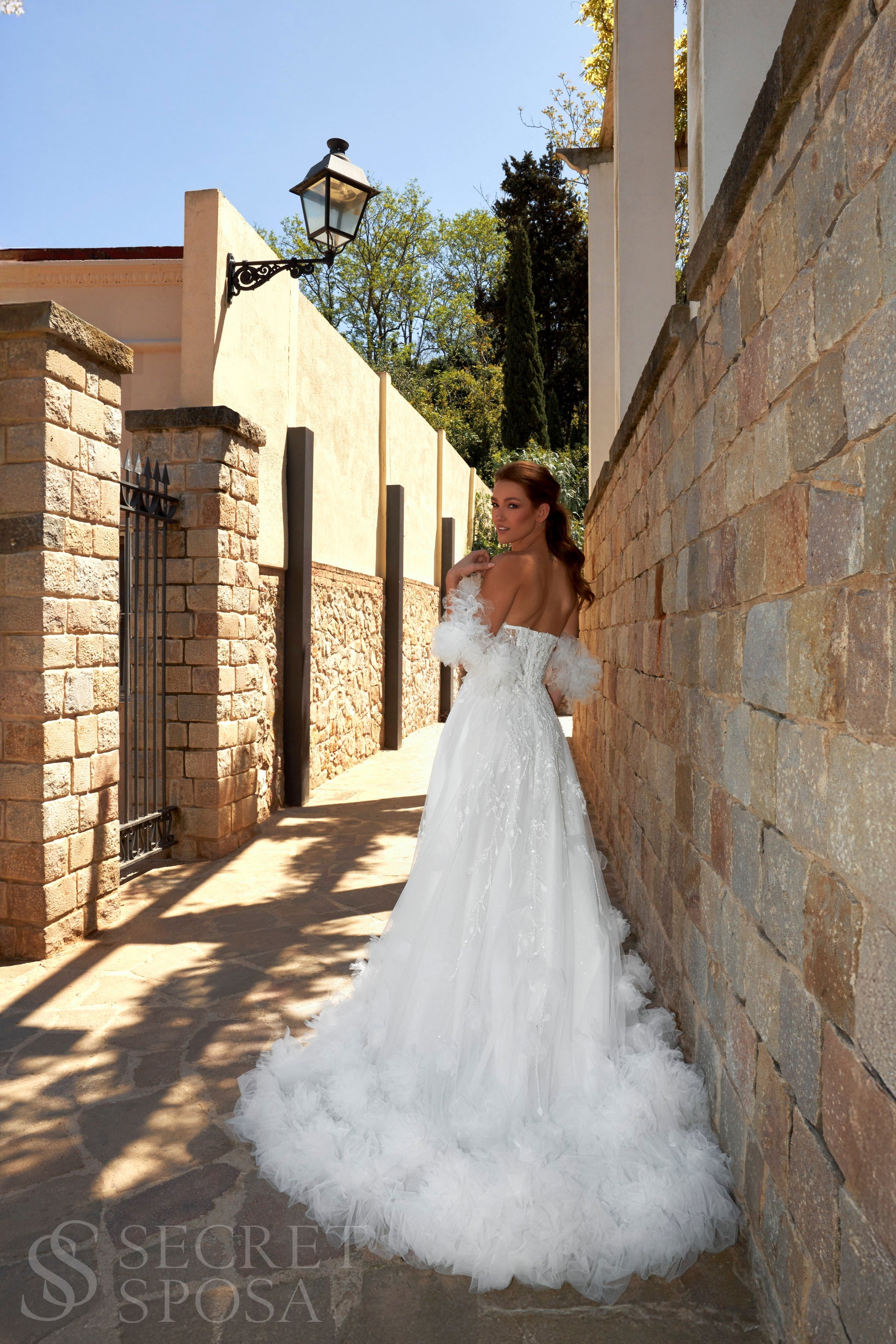 Bride in sleeveless tulle A-line wedding gown with pearl-adorned lace, 3D floral appliqués, boat neckline, slit skirt, drop waist, and straight open back.