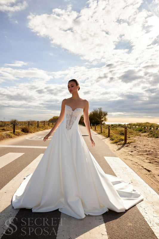 Bride in classic A-line atlas wedding gown with lace detail, V-cut neckline, drop waist, straight zip-closure back, and chapel train.