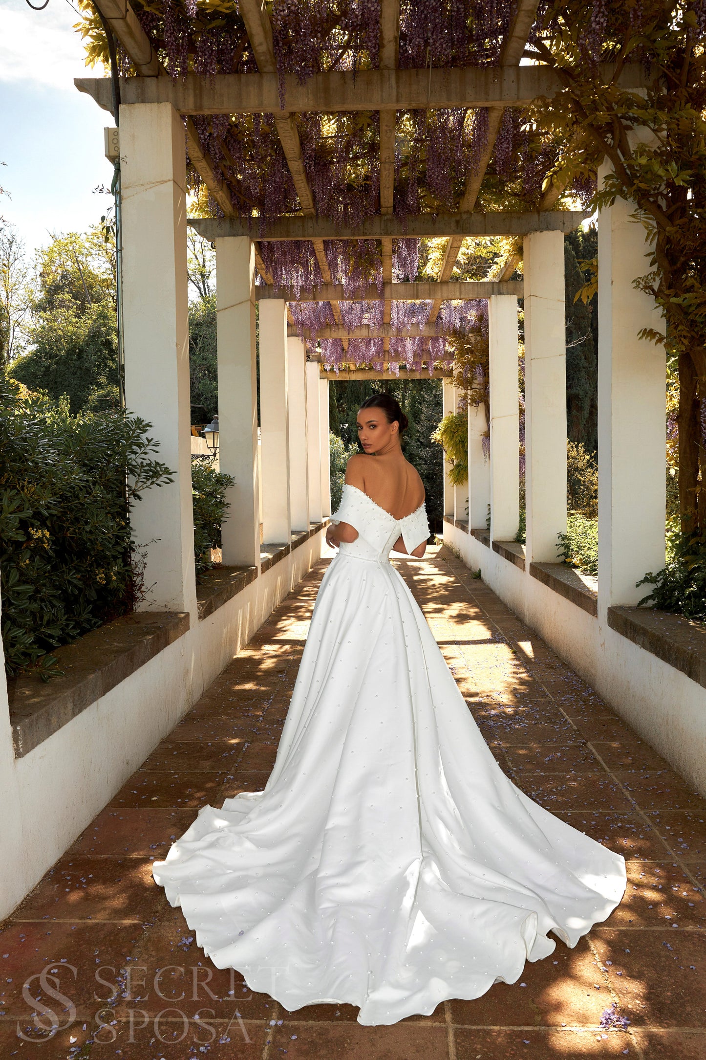 Bride in plain Mikado A-line wedding gown with pearl details, off-the-shoulder crossed bodice, chapel train, and zip closure.