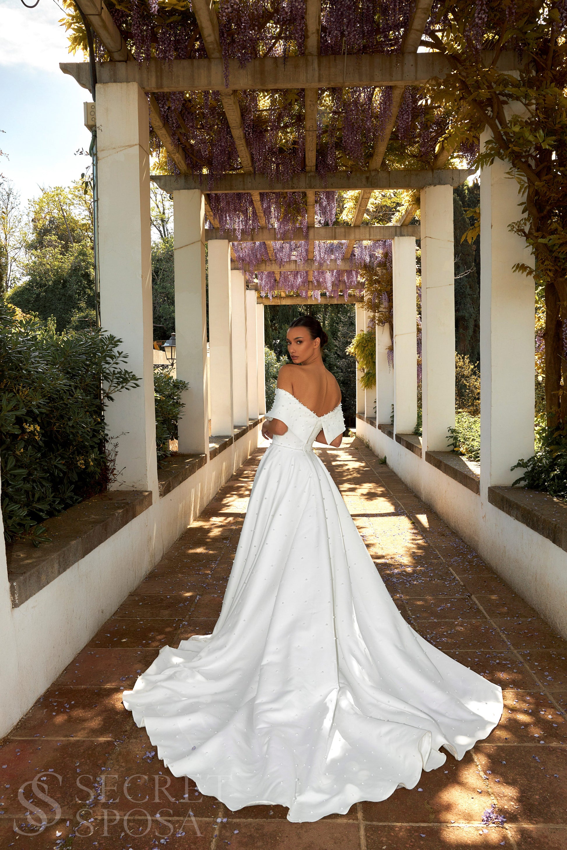Bride in plain Mikado A-line wedding gown with pearl details, off-the-shoulder crossed bodice, chapel train, and zip closure.