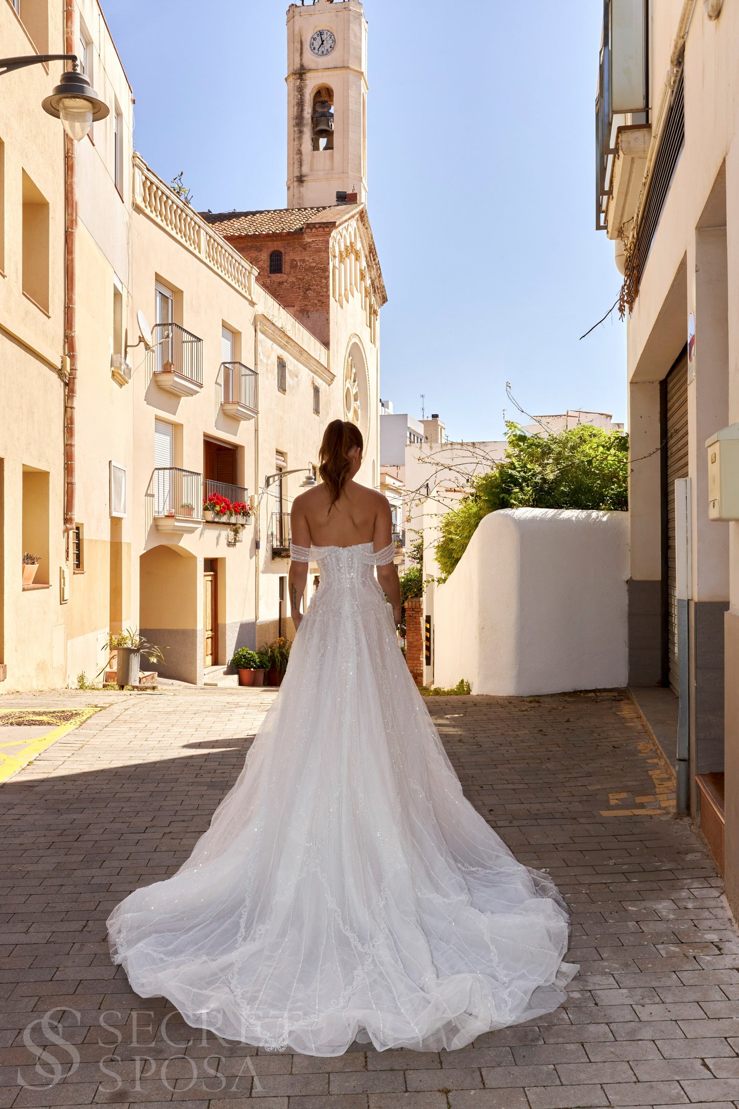 Bride in A-line tulle wedding dress with pearl and sequin embroidery, V-neckline, removable long off-the-shoulder sleeves, straight open back, and chapel train.