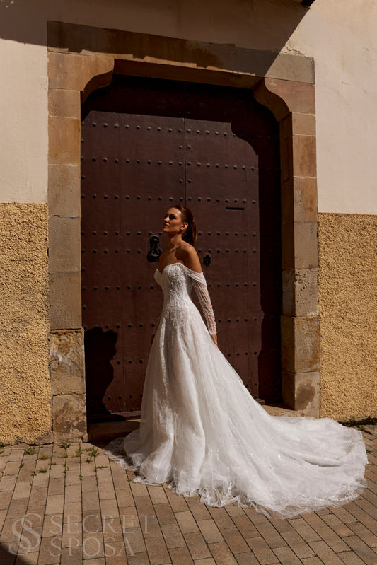 Bride in A-line tulle wedding dress with pearl and sequin embroidery, V-neckline, removable long off-the-shoulder sleeves, straight open back, and chapel train.
