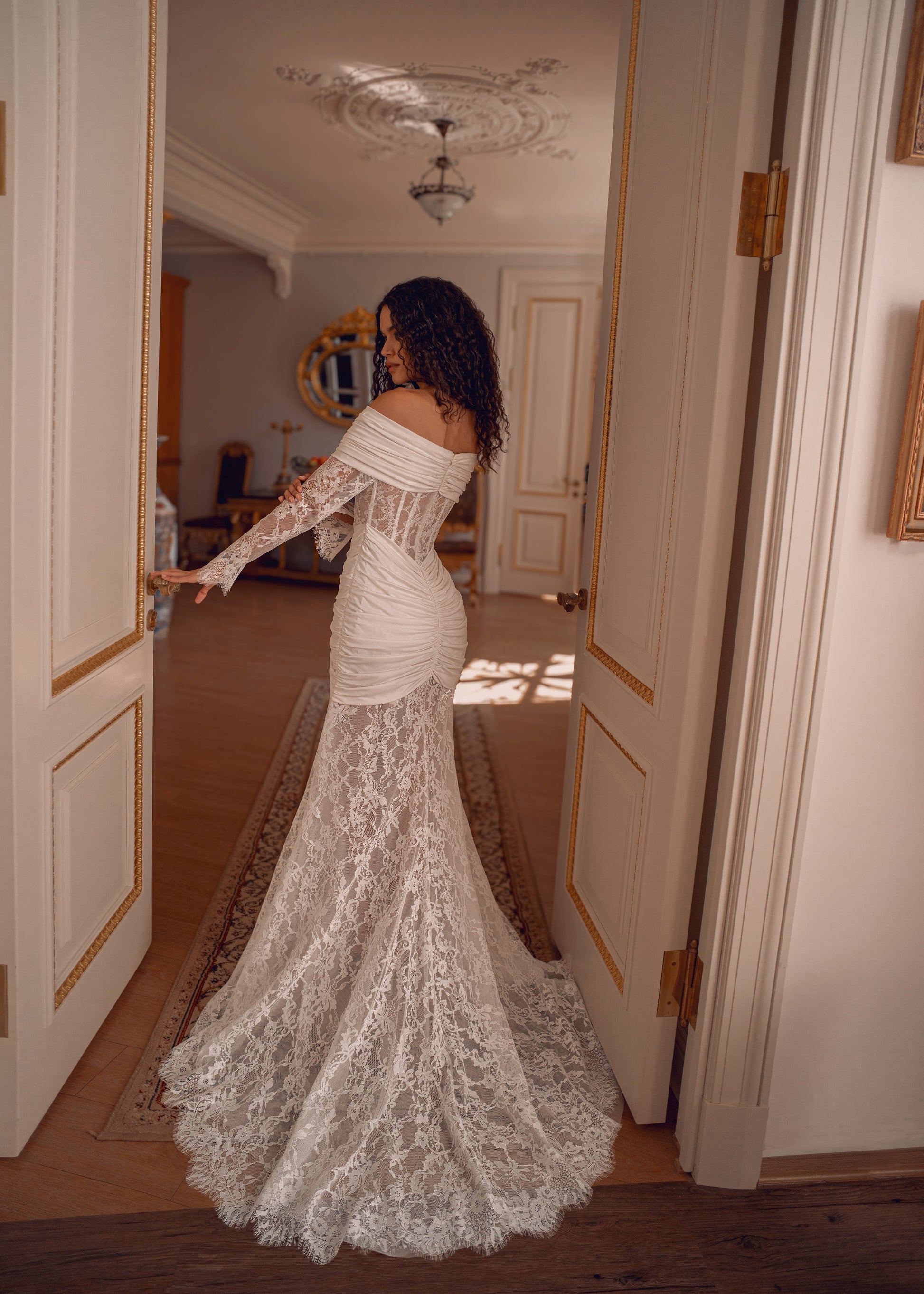 Off-shoulder lace wedding gown with draped satin details and corset bodice.