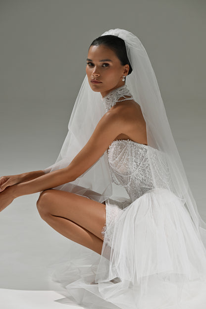 Lace mini wedding dress with corset bodice – model crouching with the veil and tulle train