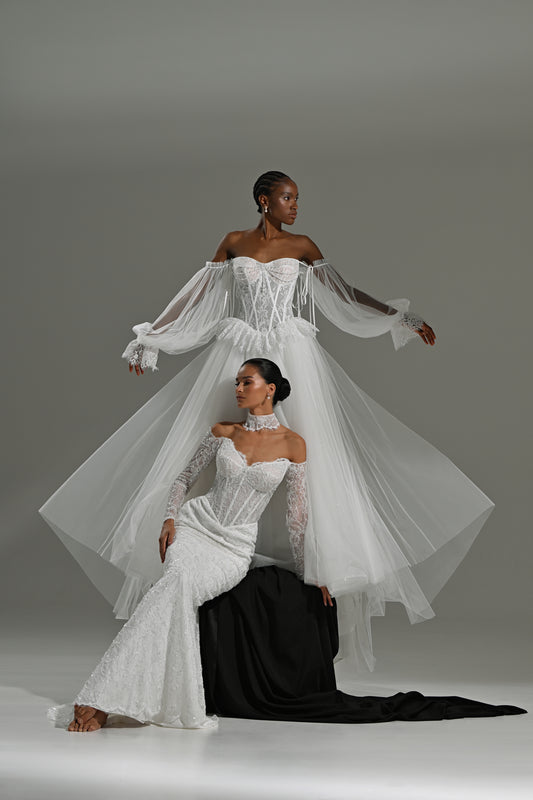 Lace and tulle ball gown wedding dress with corset bodice and peplum waist – two brides, one standing in the tulle overskirt and one seated on a black block