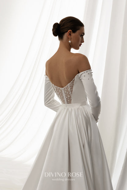 Off-shoulder satin wedding dress with long sleeves and slit.